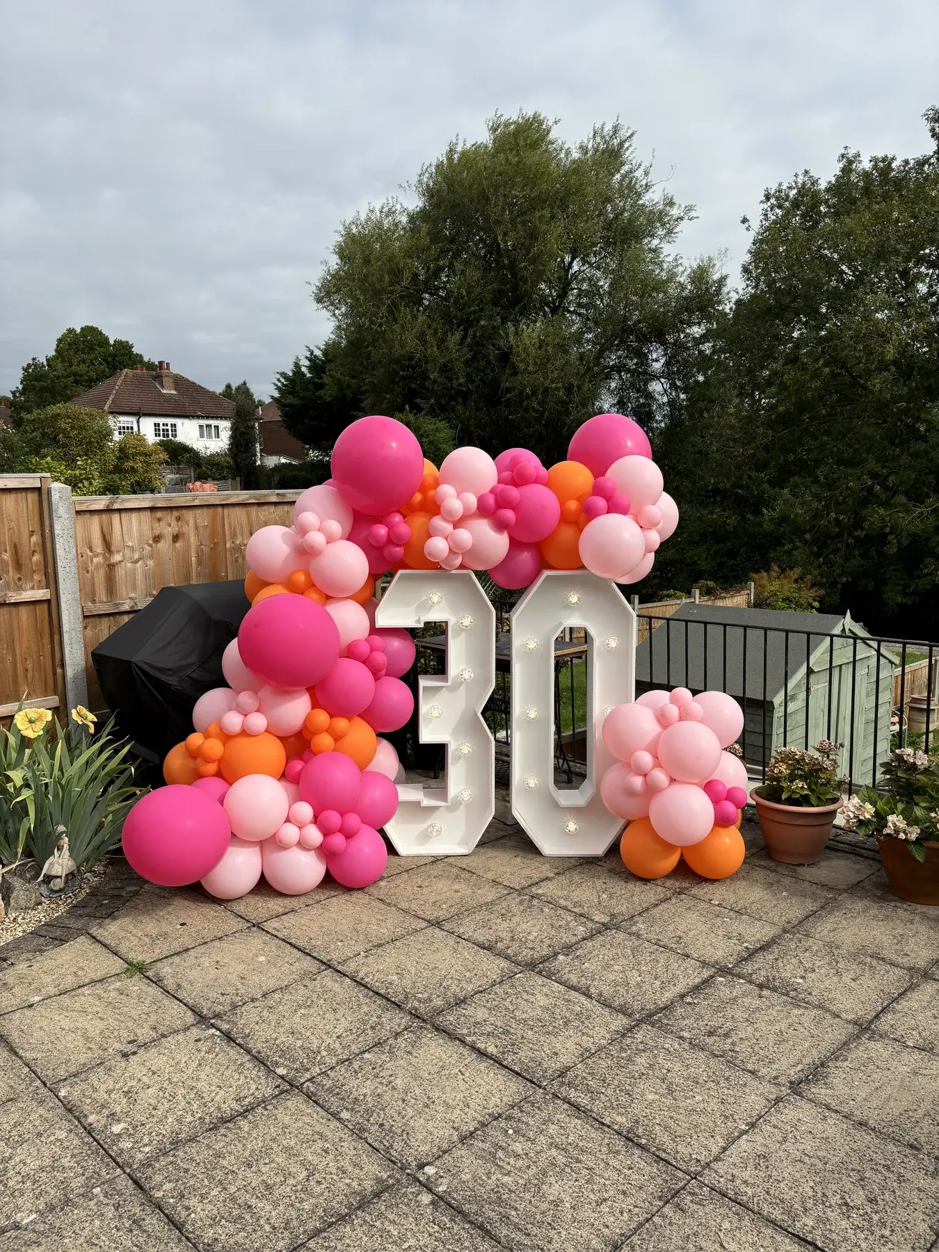 Bright pink balloon display framing illuminated number thirty at an outdoor celebration